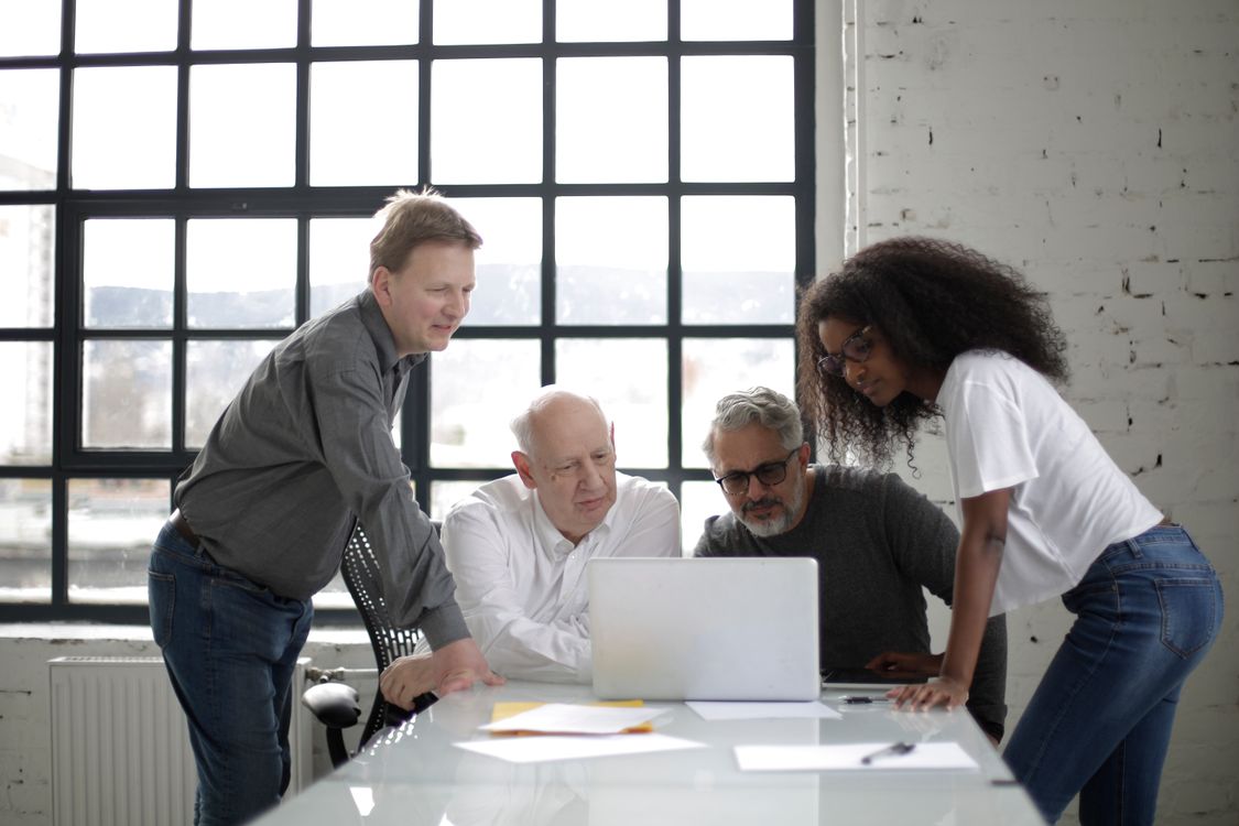 Colleagues in casual clothing collaborating around a laptop in a bright workspace.